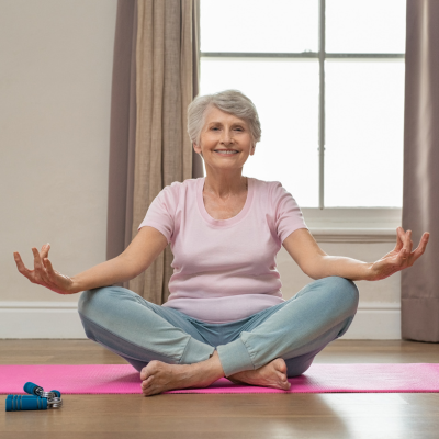 Elderly woman smiling and sitting on a mat performing yoga exercises.